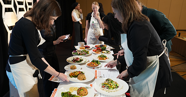 people wearing aprons looking over a table on stage with plates of healthy foods